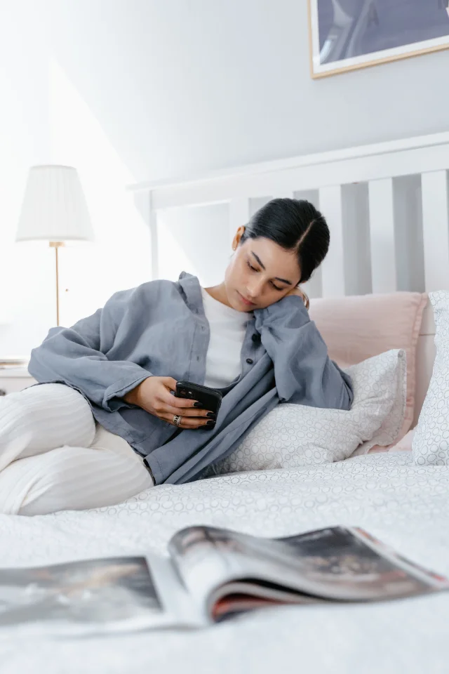 Someone sitting on the edge of a bed at home, phone in hand, part-way through the day.